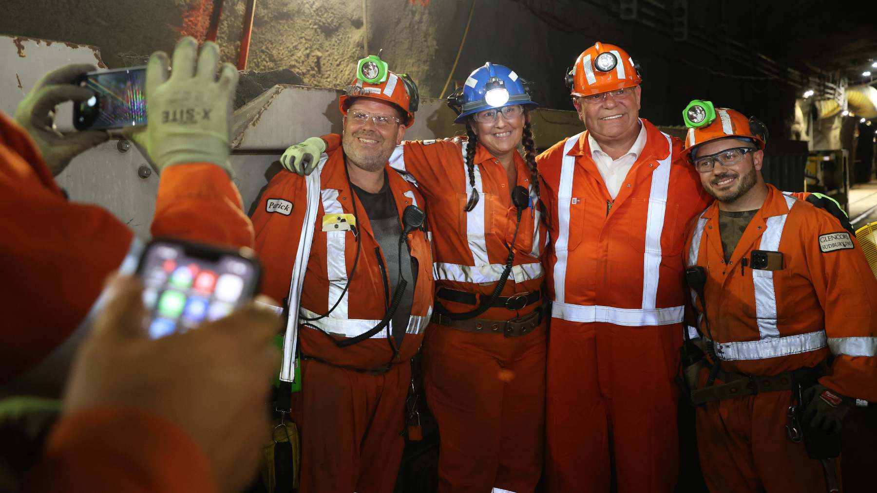 Trabajadores con casco y mono naranja celebran bajo tierra el acceso al yacimiento de Onaping Depth