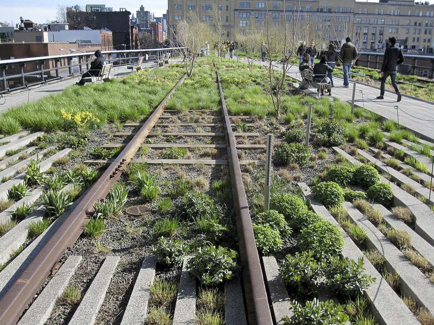 Raíles originales entre parterres de hierbas y arbustos en el parque de la High Line, con paseantes