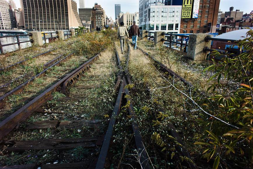 Dos personas caminan entre vías de la High Line cubiertas de vegetación espontánea en los Rail Yards