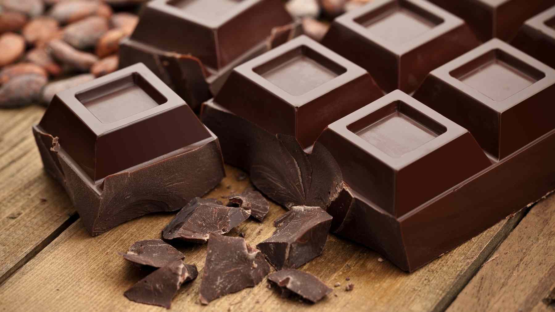 Tabletas de chocolate negro con trozos y granos de cacao sobre una mesa de madera