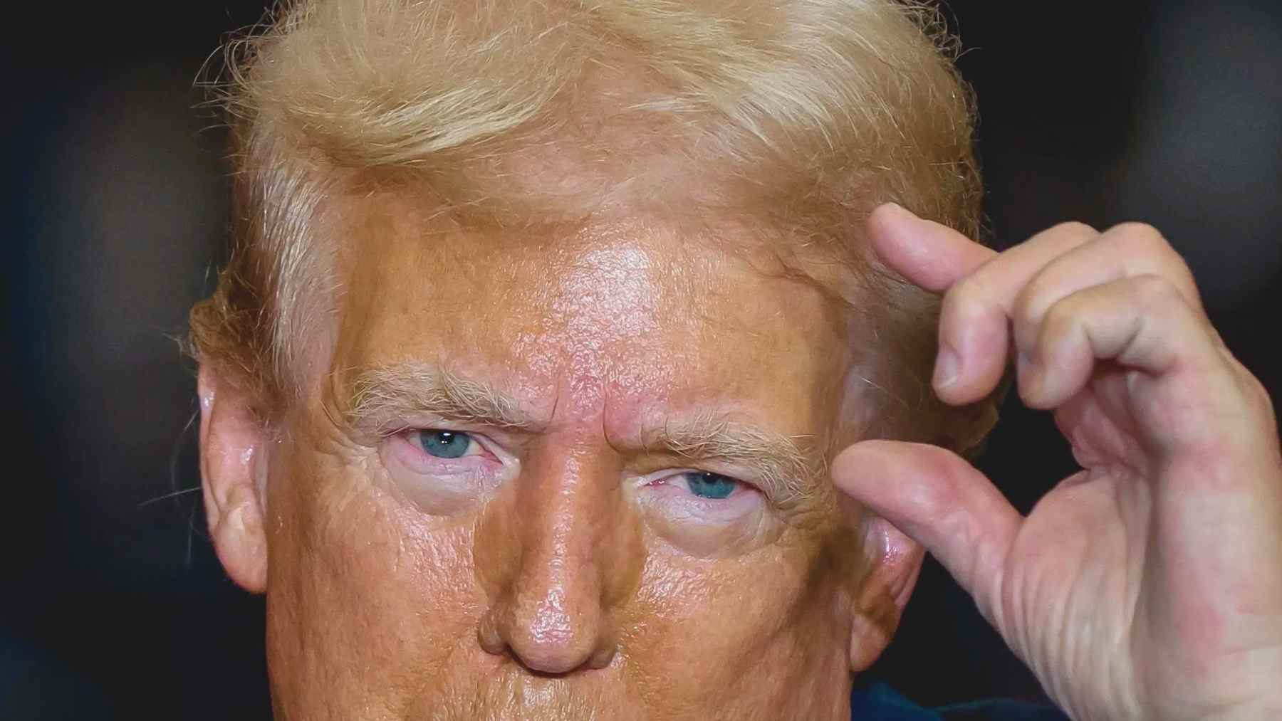 Donald Trump, en primer plano, realiza un gesto con la mano durante un acto en interior.