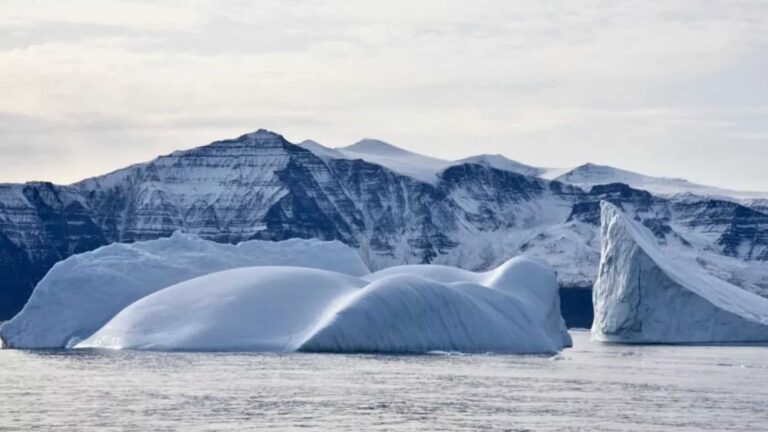 Gran iceberg flotando en aguas polares con montañas nevadas al fondo