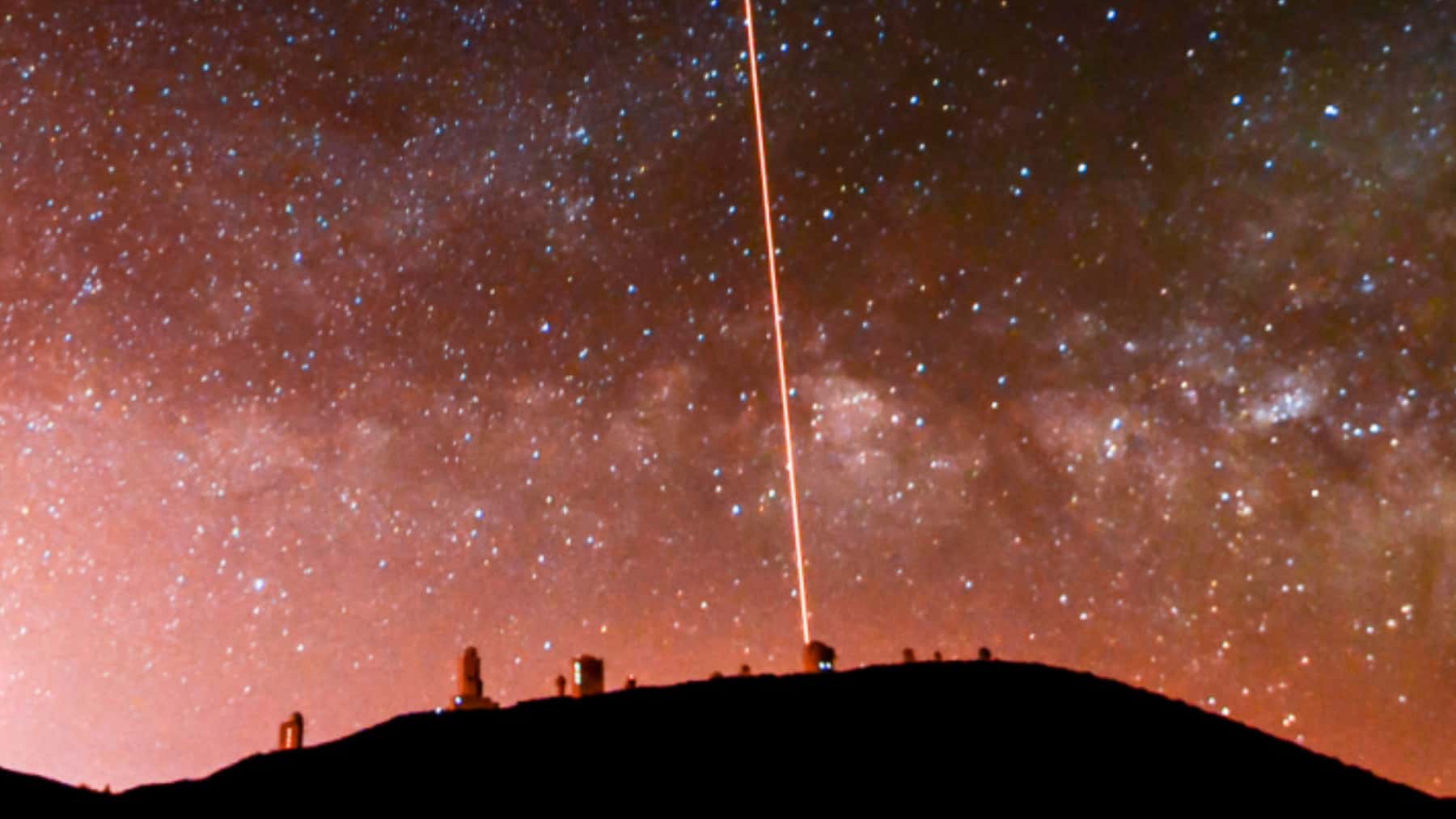 Observatorio astronómico bajo la Vía Láctea con un haz de luz láser apuntando al cielo