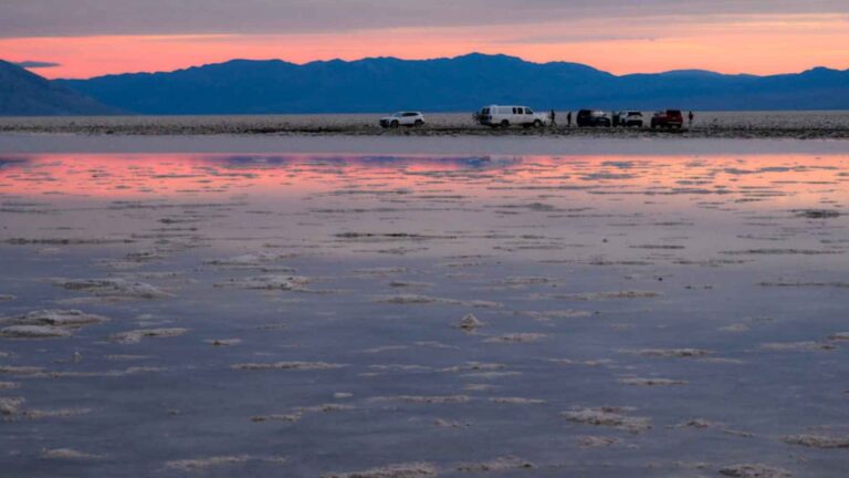 Vehículos en una llanura salina al atardecer con reflejos en el agua, imagen asociada al aumento de temperaturas globales