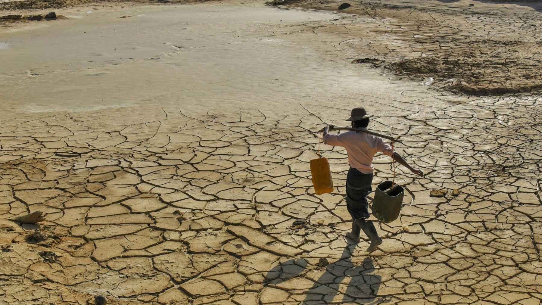 Persona caminando sobre un terreno agrietado por la sequía extrema causada por la escasez de agua