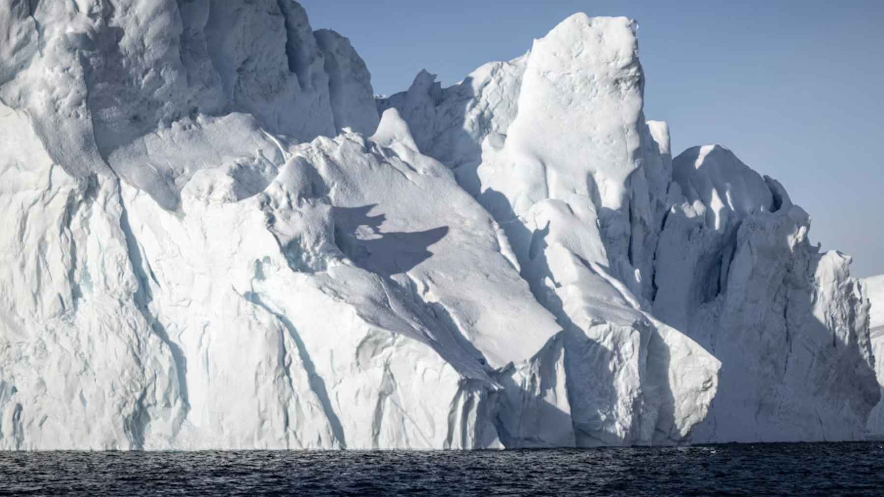 Iceberg gigante en el Ártico sobre el mar, con paredes de hielo y cielo despejado.