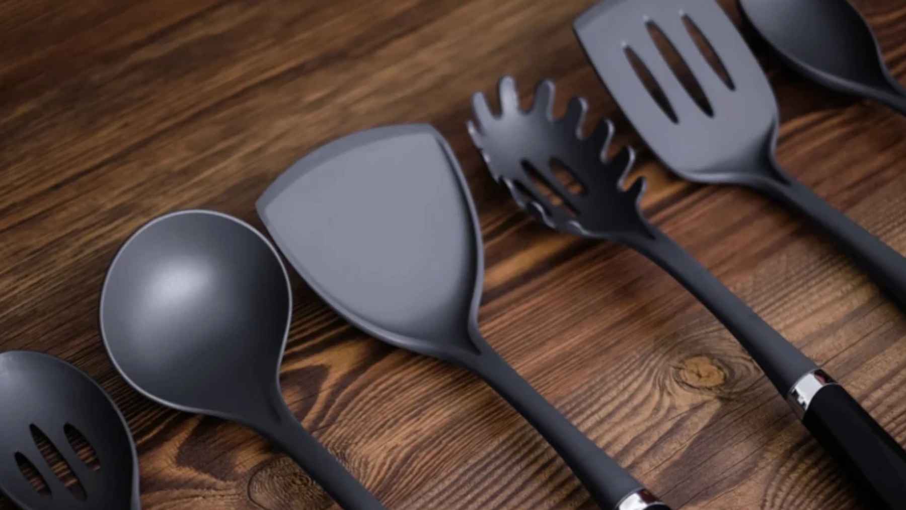 Utensilios de cocina negros de plástico sobre mesa de madera (espátula, cucharón y pala ranurada)