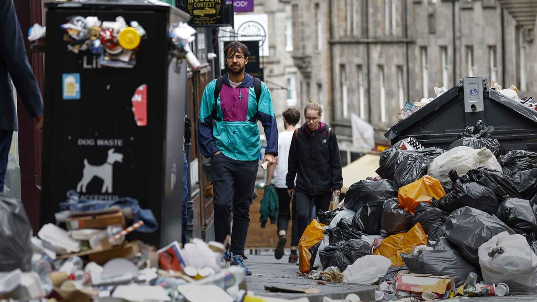 Montones de basura plástica desbordando contenedores en una calle urbana, símbolo del colapso del sistema de residuos