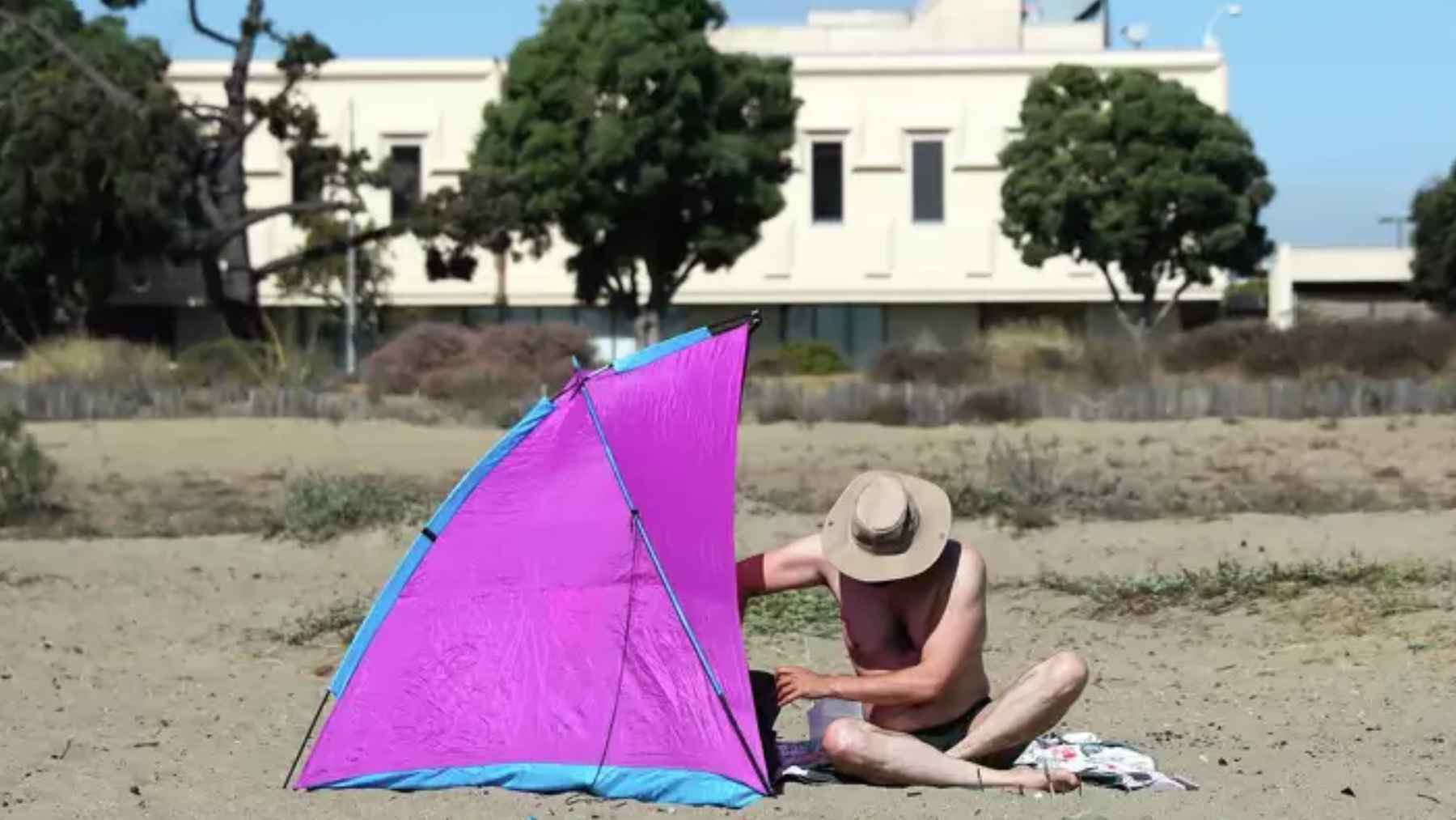 Hombre mayor se protege del sol con una sombrilla en una playa durante una ola de calor.