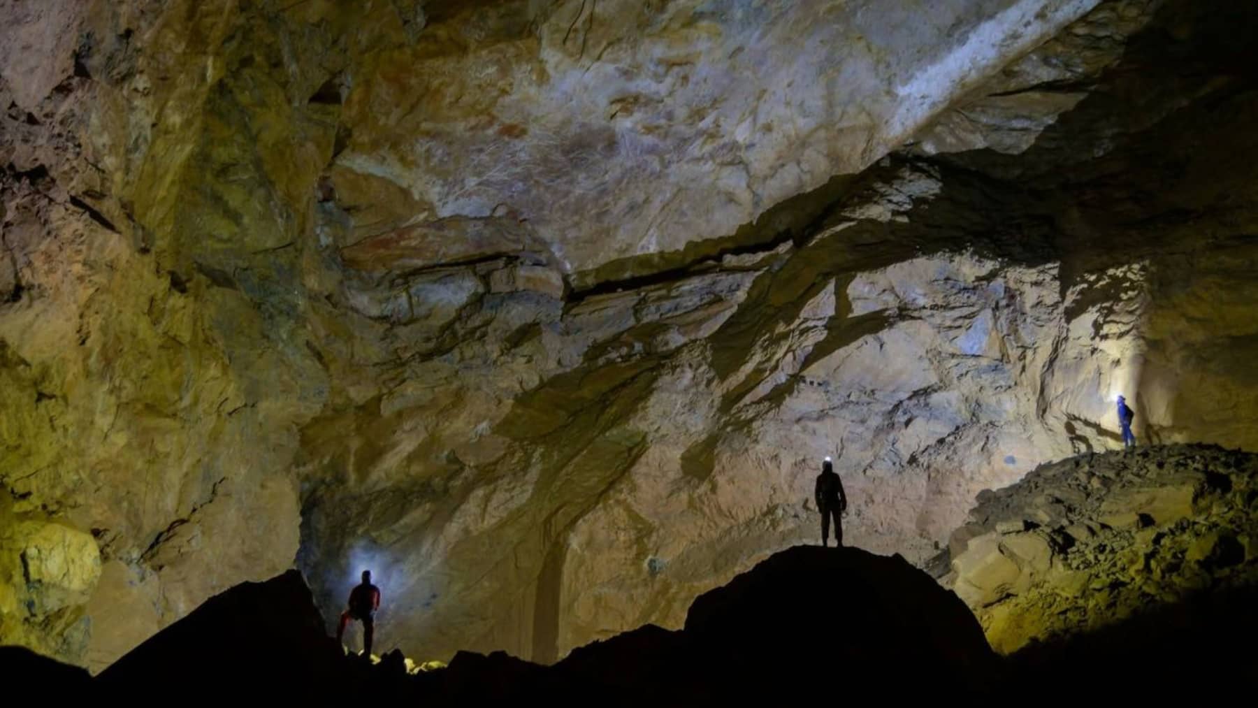 Espeleólogos con linternas dentro de una gran cueva, iluminando las paredes rocosas en una cavidad subterránea.