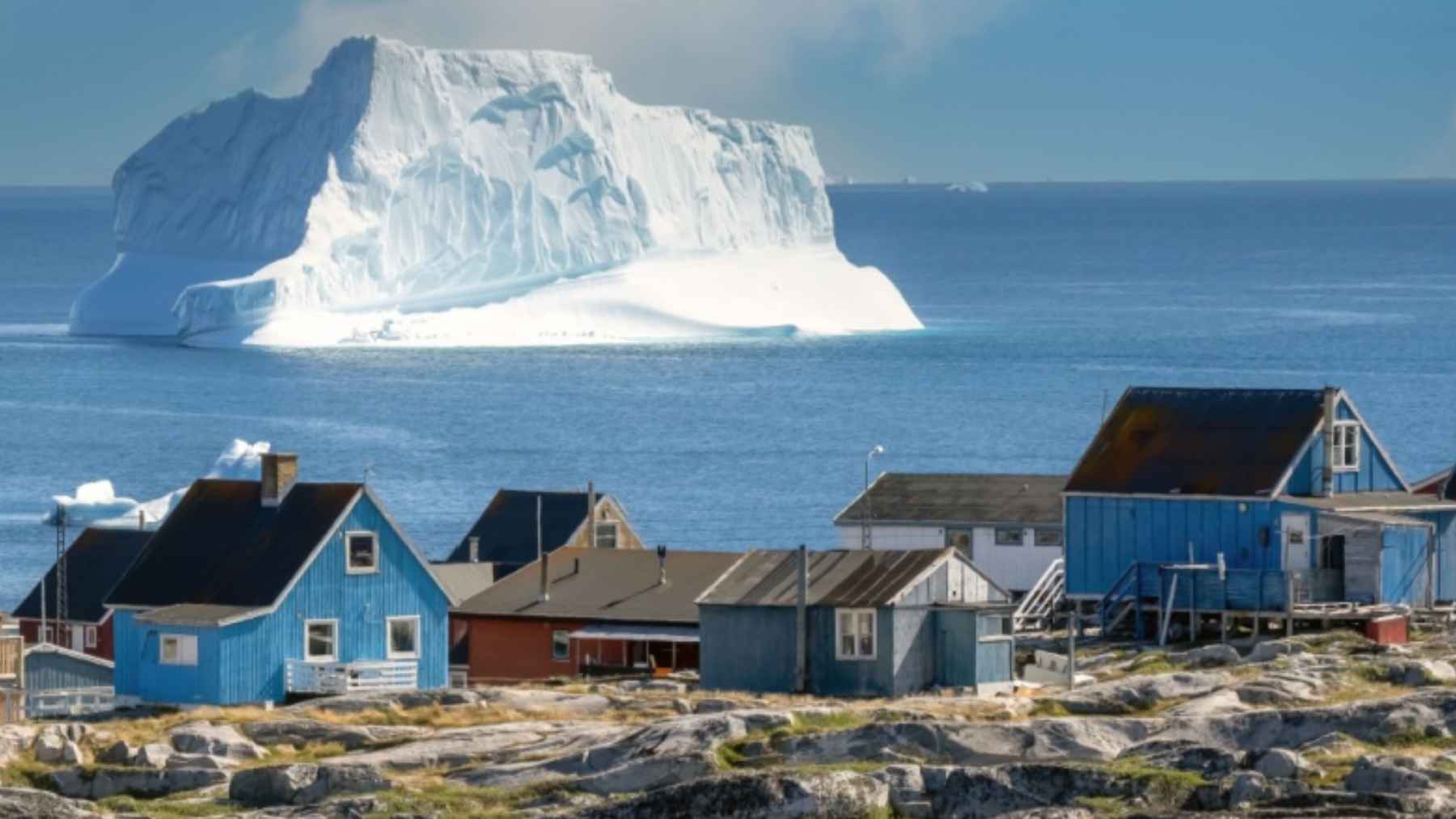 Iceberg frente a un pueblo costero de Groenlandia, símbolo del deshielo que facilita explorar tierras raras y otros recursos.