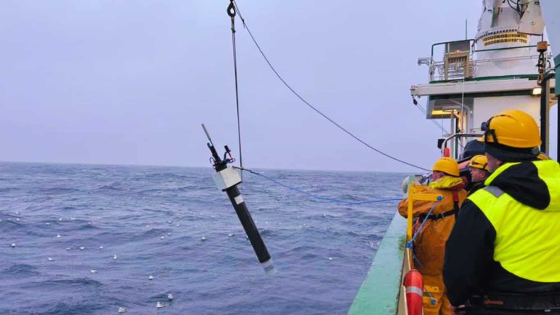 Equipo en un barco desplegando un instrumento oceanográfico de medición en el mar con grúa y cable.