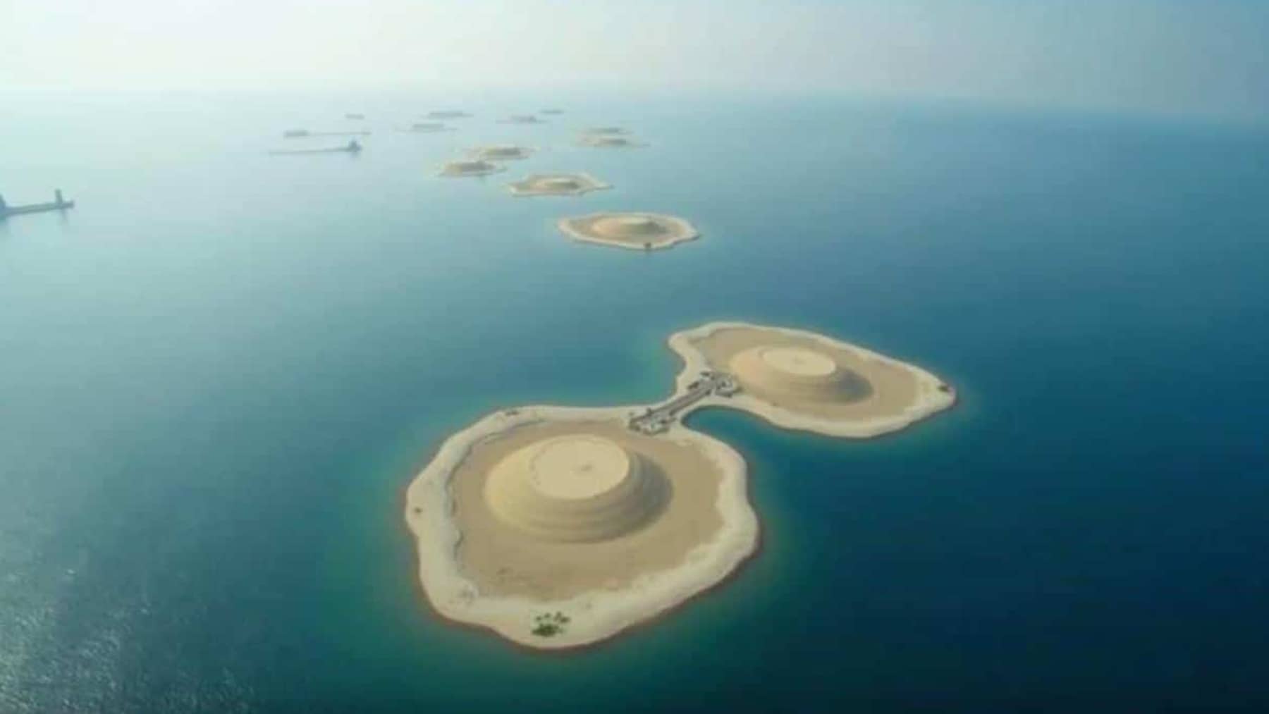 Vista aérea de varias islas artificiales construidas con arena en mar abierto, con formas circulares y una pasarela que conecta dos de ellas
