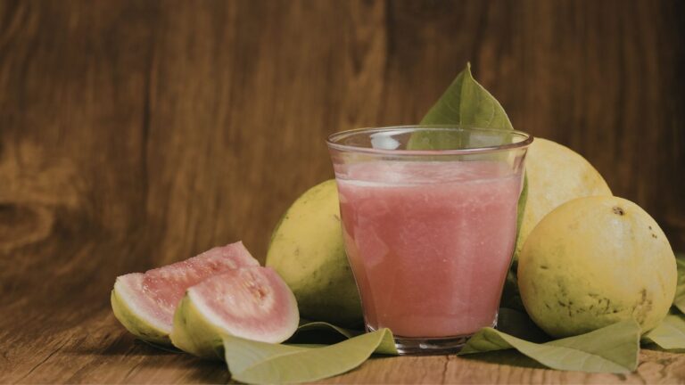 Vaso de jugo de guayaba con espinacas acompañado de guayabas frescas
