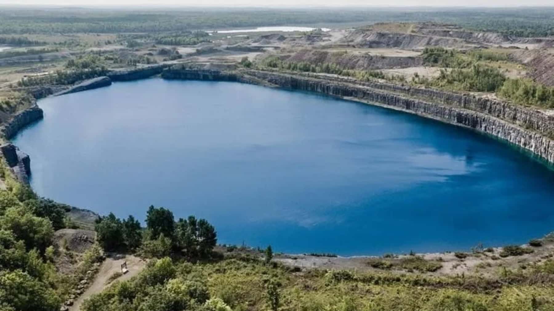 Lago artificial de agua azul en una cantera a cielo abierto, rodeado de bosque y taludes rocosos.