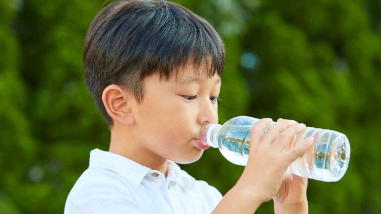 Niño pequeño bebiendo agua de una botella de plástico, potencial fuente de microplásticos.