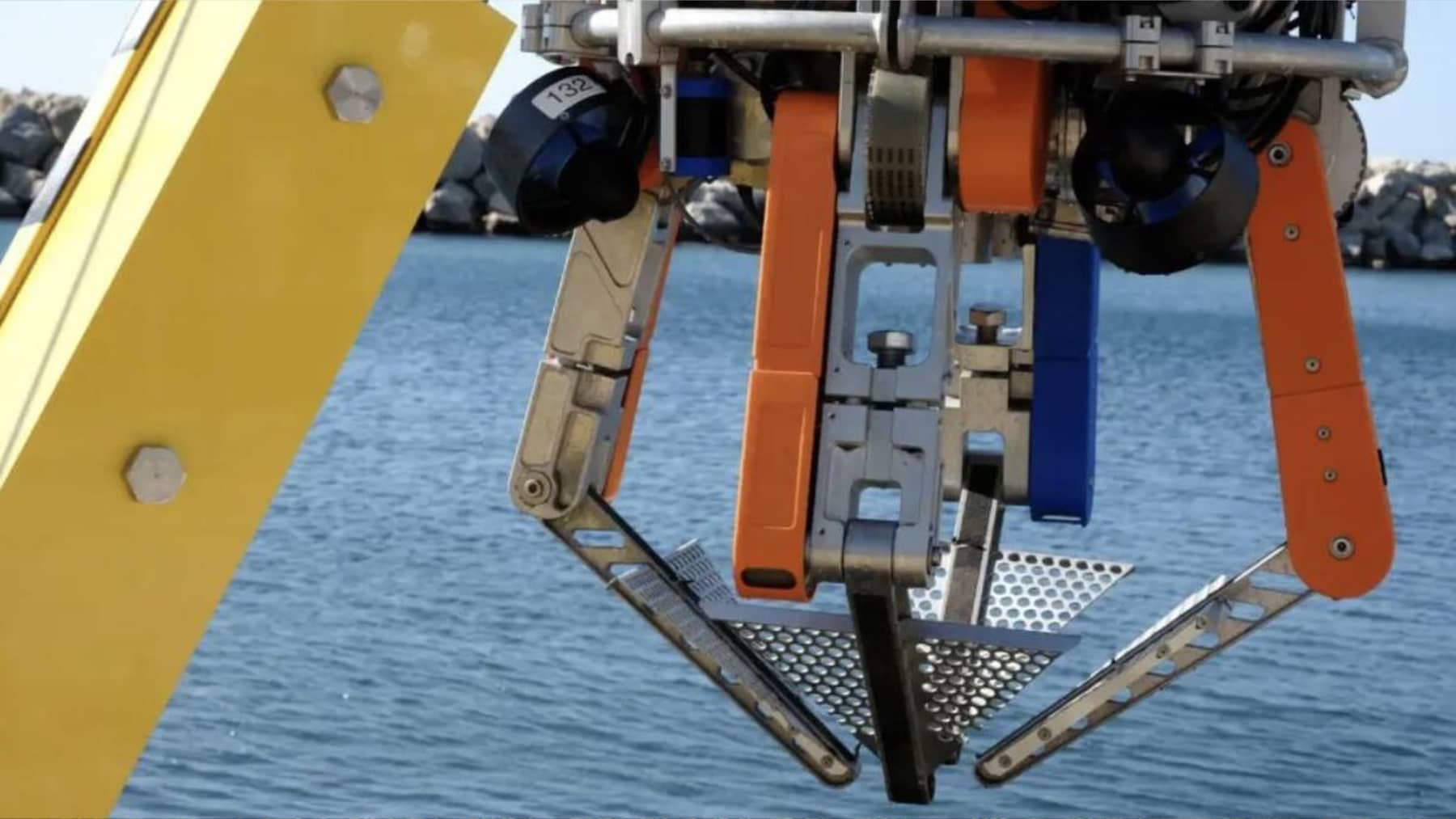 Pinza robótica industrial sobre el mar, con brazos metálicos y mecanismo de agarre para operaciones marinas.