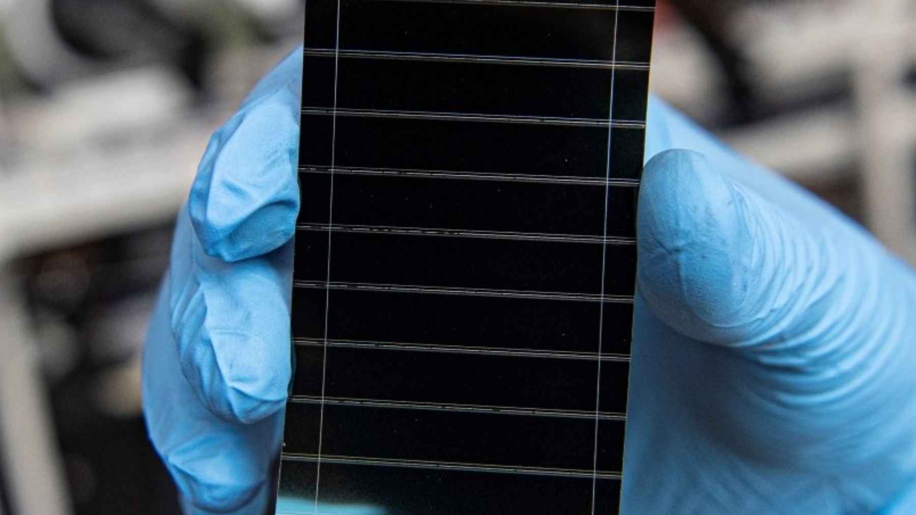 Célula solar de perovskita mejorada mediante recocido por prensado molecular, sostenida por un técnico con guantes