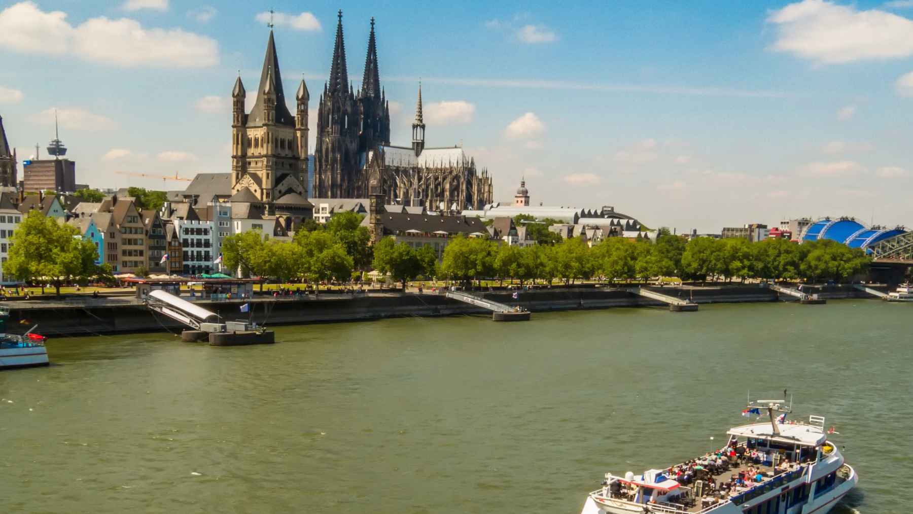 Vista del río Rin en Colonia con la catedral al fondo y una embarcación turística sobre aguas afectadas por contaminación plástica.
