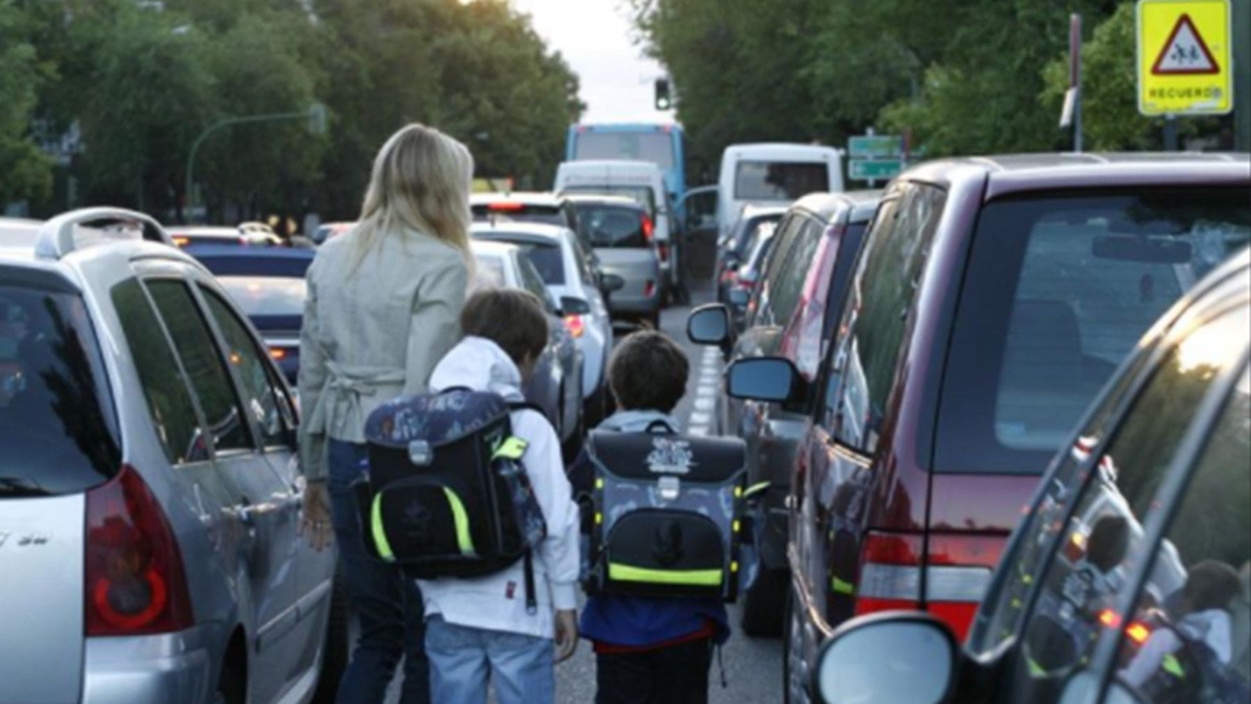 Alumnos caminando entre coches en un atasco frente a un colegio en Palma con altos niveles de contaminación por NO2.