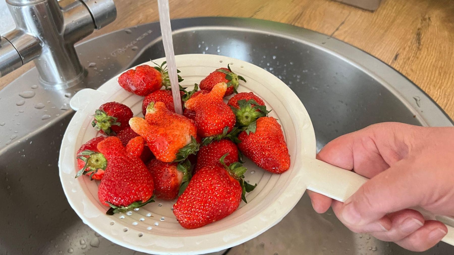 Lavando fresas bajo el grifo para reducir restos de pesticidas y suciedad antes de consumirlas.