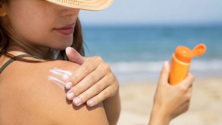 Mujer aplicándose crema con protector solar SPF 50 sobre el hombro antes de exponerse al sol en la playa.