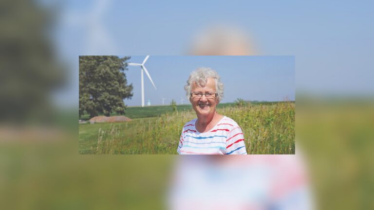 Evie, agricultora de Iowa, sonríe en su granja con uno de sus tres aerogeneradores al fondo