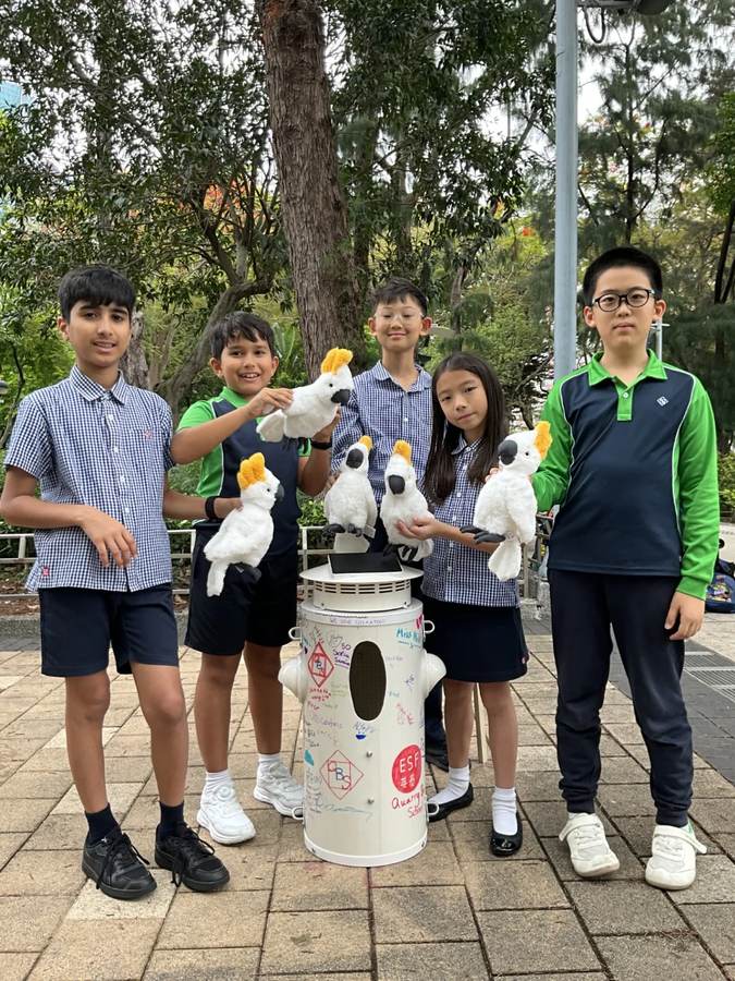 Alumnos de Quarry Bay School posan con cacatúas de peluche junto a una caja nido en Victoria Park