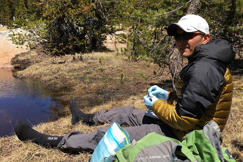 Dave Daversa con guantes azules sentado junto a una charca de montaña en Yosemite con material de muestreo