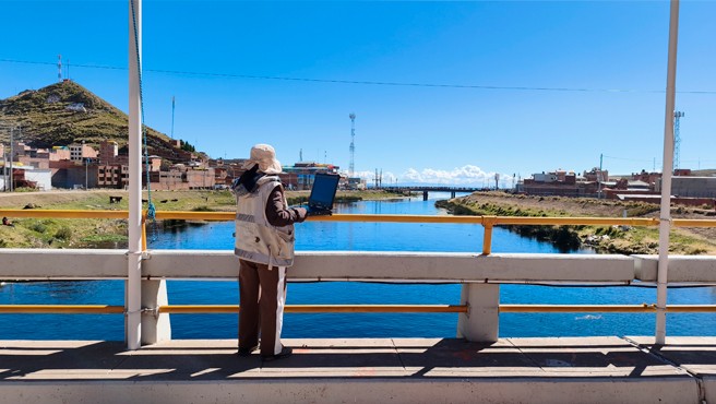 Una especialista del Senamhi trabaja con un portátil sobre un puente, en la nota oficial sobre el nivel del lago Titicaca