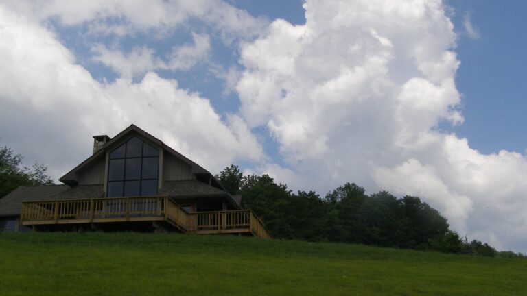 Casa de madera con grandes ventanales sobre una pradera bajo un cielo con nubes Great Smoky Mountains